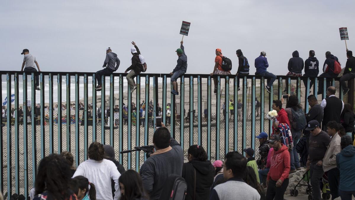 Central American immigrants traveling with a caravan gather at the border wall as some sit on top of it, looking toward the U.S. from Tijuana, Mexico, on April 29.