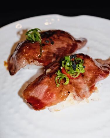 A vertical photo of two scallion-topped pieces of Wagyu nigiri on a white plate at Moohan Korean BBQ in Koreatown