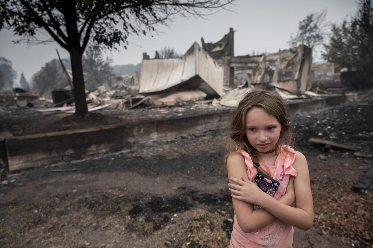 Ellie Owens, 8, looks at fire damage Friday as destructive wildfires devastate the region.