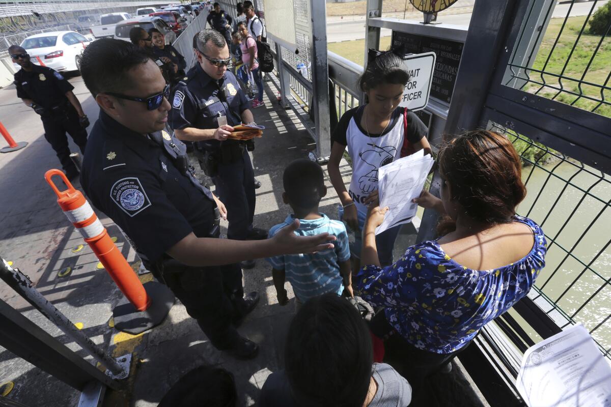 Un oficial de Aduanas y Protección Fronteriza de los Estados Unidos revisa los documentos de los migrantes antes de ser llevados a solicitar asilo en Estados Unidos, en el Puente Internacional 1 en Nuevo Laredo, México, la semana pasada. (Marco Ugarte / Associated Press)