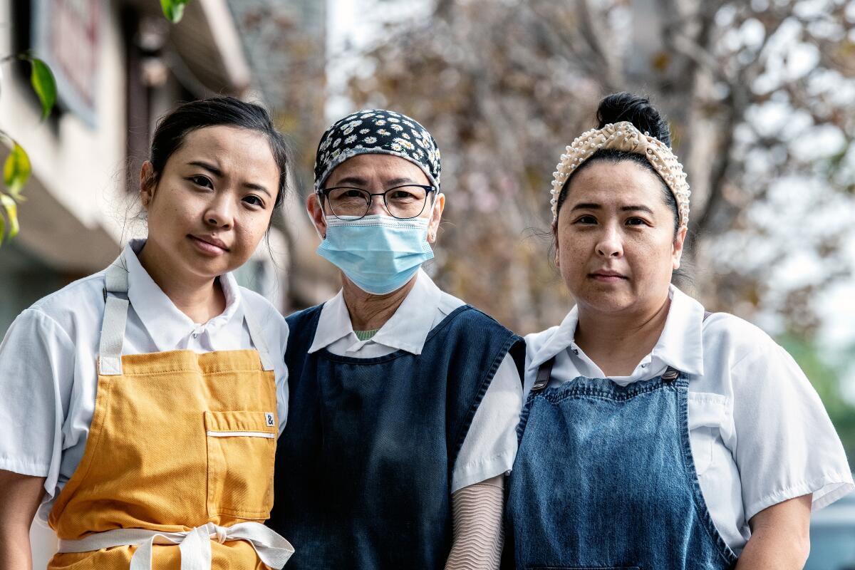 Three women stand, wearing aprons