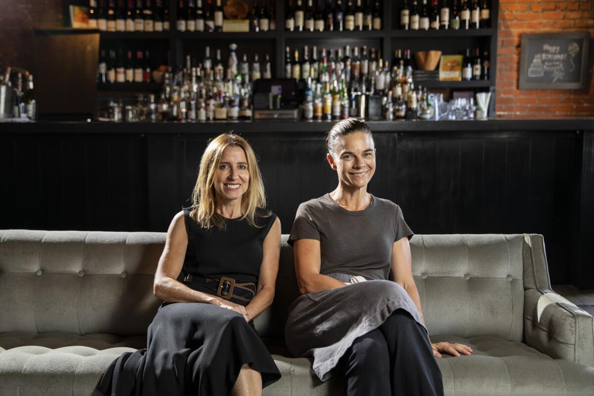 Caroline Styne and Suzanne Goin sit on a couch in front of a bar