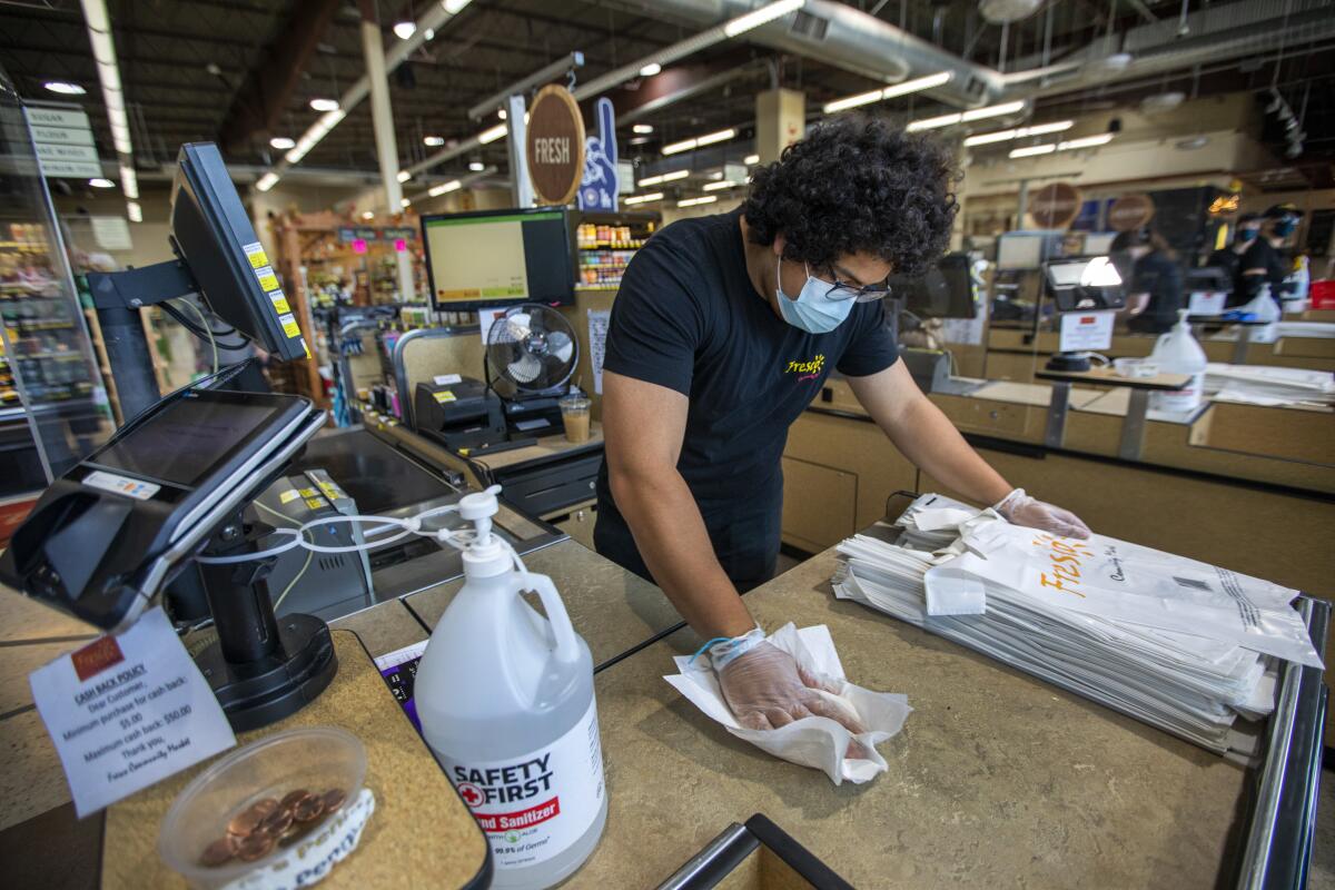 A worker wearing a mask cleans a grocery store counter