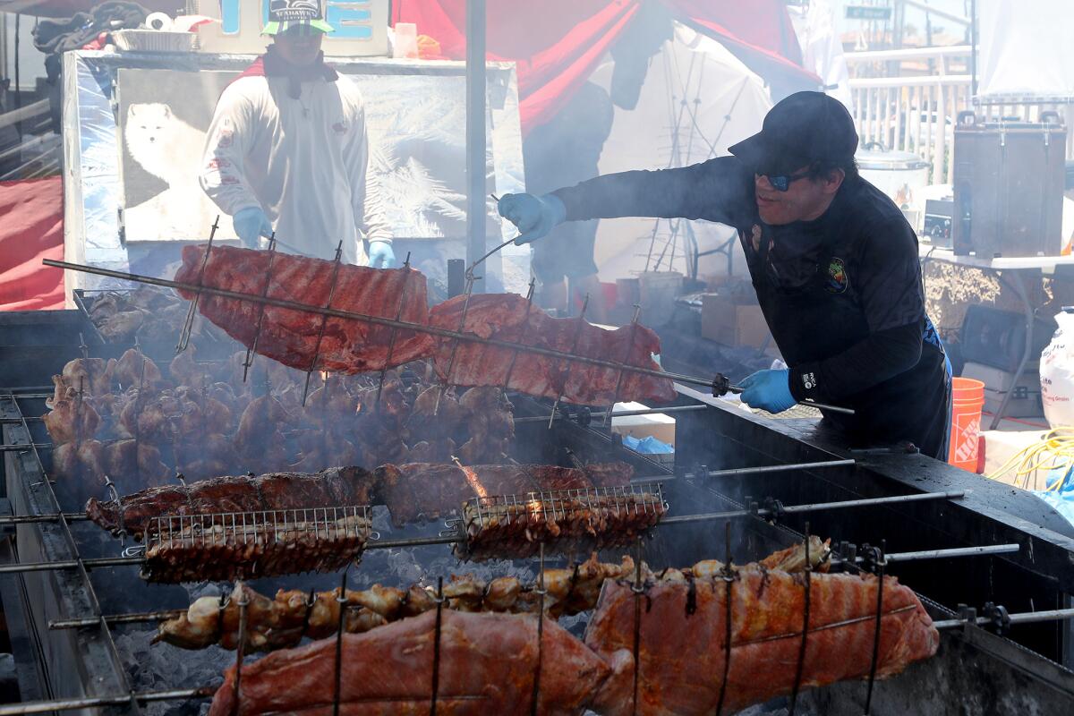 A Hawaiian Dancing Grill BBQ cook adds ribs to the grill during Pier Plaza Festival on Saturday in Huntington Beach.