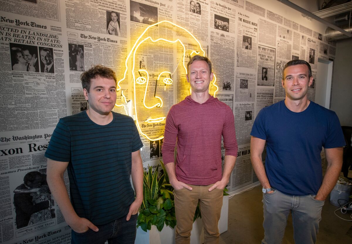 Three young men stand in front of a wall decorated with newspapers.