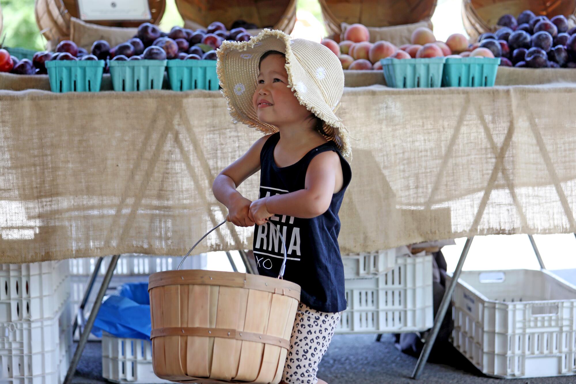 Ellis Cabie, 2, helps her mom pick out fruit at the Farmers Market in Irvine Regional Park on Tuesday.