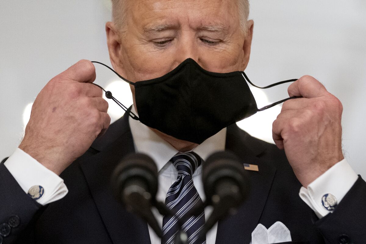 President Biden takes off his mask to speak at two microphones.