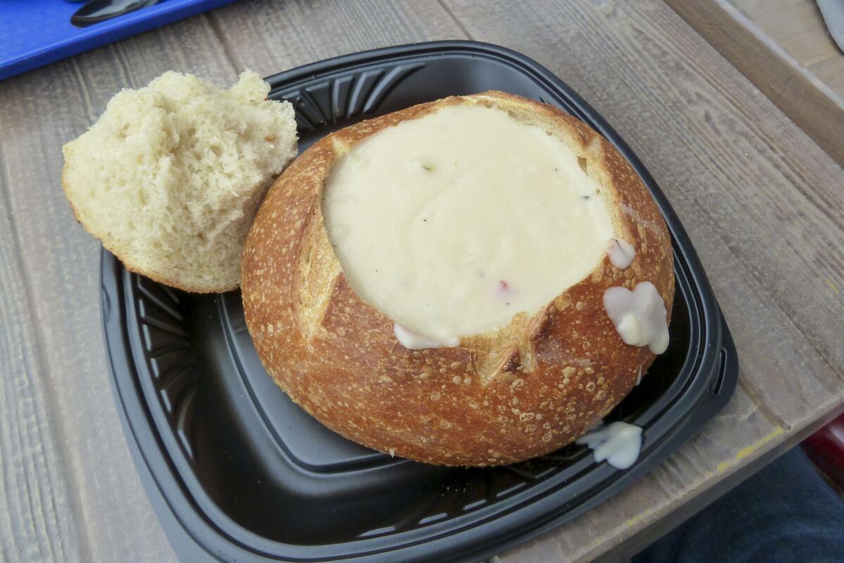 Clam chowder in sourdough bread bowl sits on a wooden table.