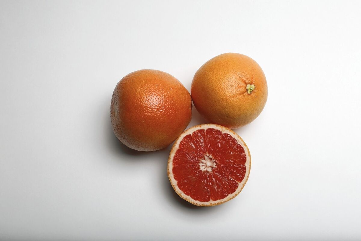A still life of whole and cut grapefruit on a white background