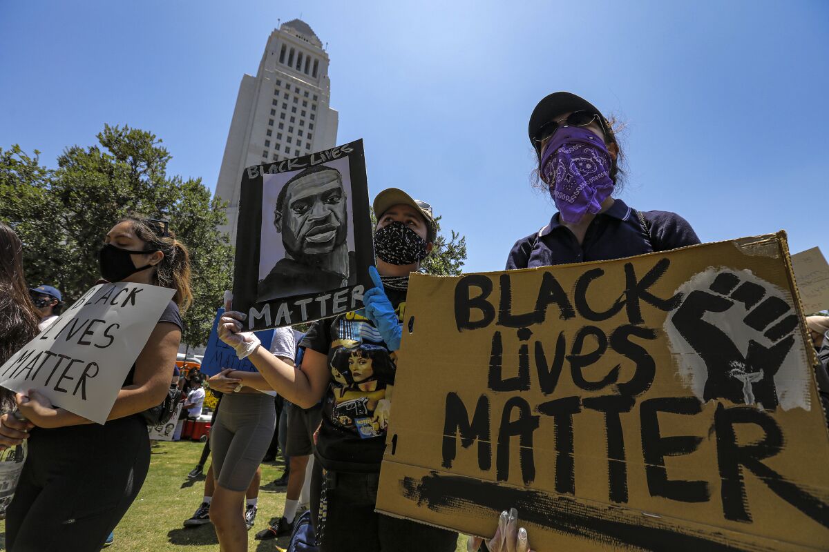 Protesters hold signs that say "Black lives matter" and have George Floyd's image.