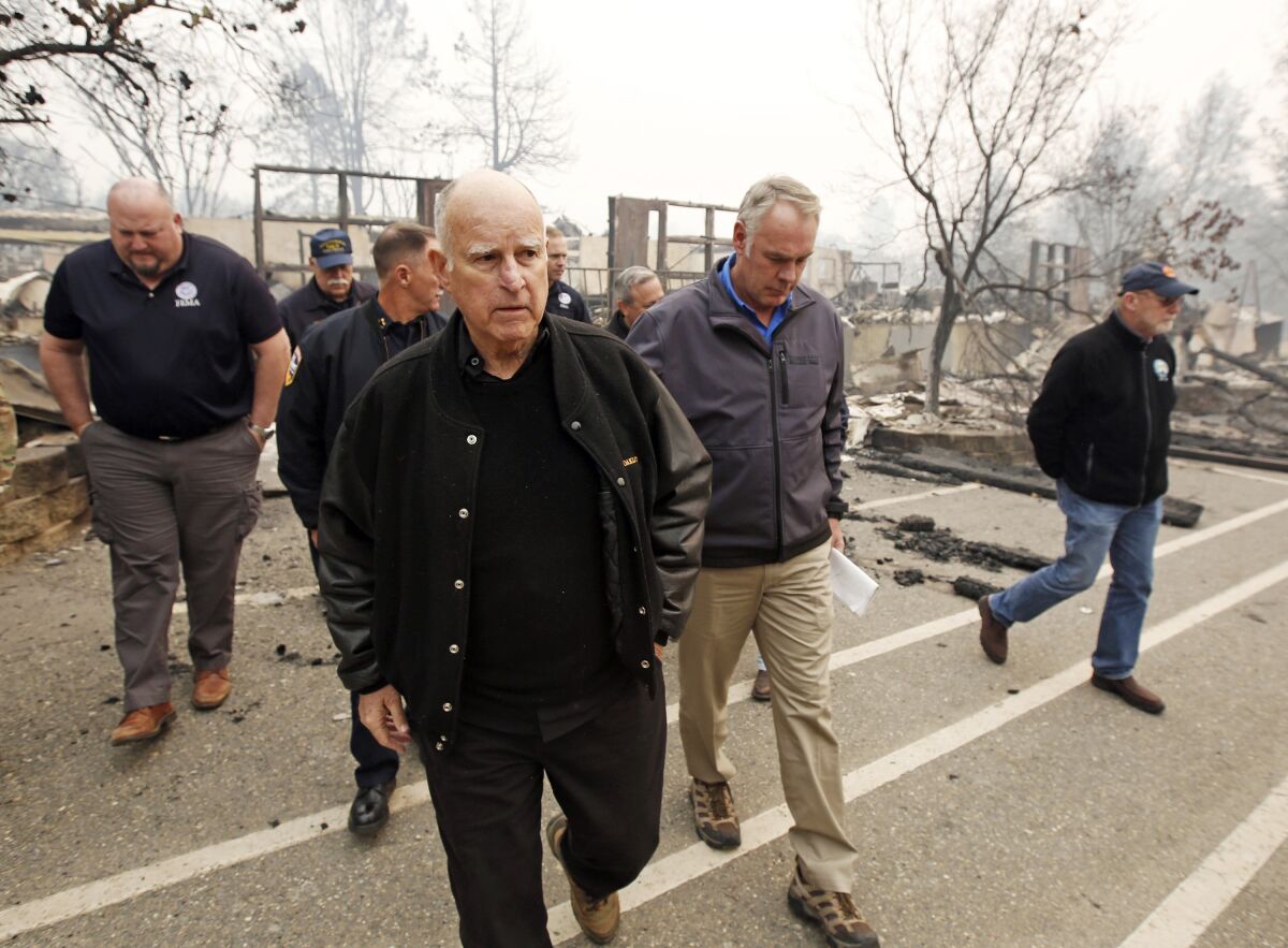 FILE - Former California Gov. Jerry Brown, center, and former Interior Secretary Ryan Zinke, second from right, tour the Camp-fire ravaged Paradise Elementary School in Paradise, Calif., on Nov. 14, 2018. Brown has called California's mega fires "the new abnormal" as climate change turns the state warmer and drier. With the help of Ken Pimlott, the former chief of the California Department of Forestry and Fire Protection, Brown convened a group at his rural Colusa County ranch in September 2021, to discuss what could be done to save California's forests. (AP Photo/Rich Pedroncelli, File)