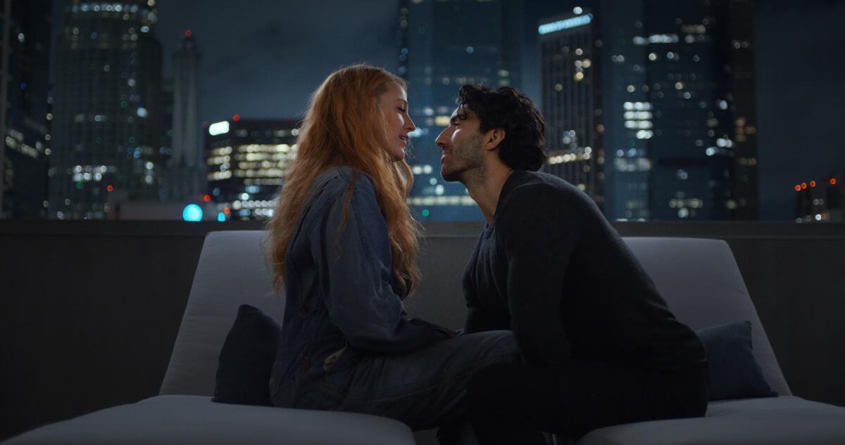 Blake Lively and Justin Baldoni leaning in for a kiss on a couch on a rooftop overlooking a city skyline