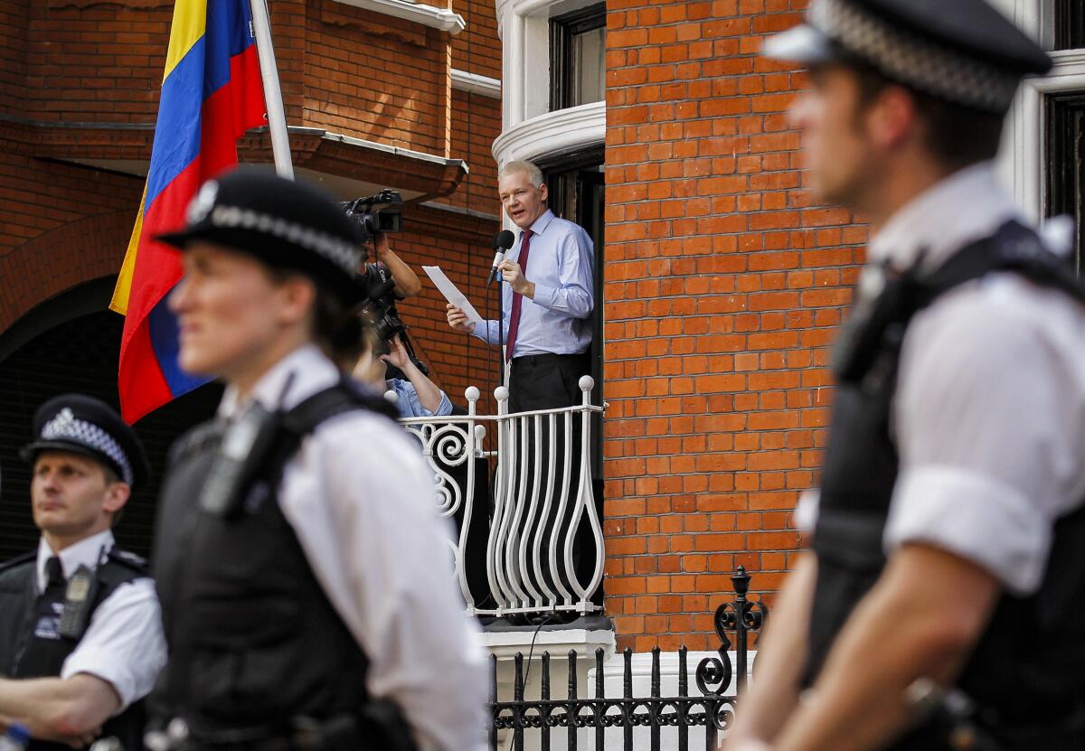 FILE - British police stand guard as WikiLeaks founder Julian Assange, center, address media and supporters from a window of the Ecuadorian Embassy in central London, Aug. 19, 2012. Two lawyers and two journalists are suing the CIA, saying the agency obtained copies of the contents of their electronic devices and helped enable the recording of their meetings with Assange, during the latter part of his seven-year stay at the embassy. The plaintiffs seek compensatory and punitive damages in a lawsuit filed Monday, Aug. 15, 2022 in Manhattan federal court.(AP Photo/Sang Tan, File)