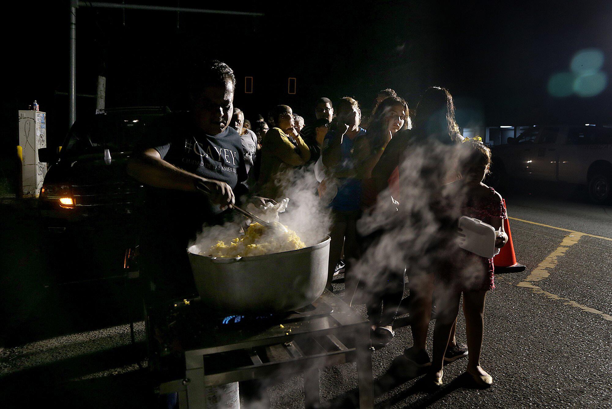 Jose Rosario, a municipal employee, cooks for residents in the town of Guayanilla on the southern coast of Puerto Rico as they lined up to get hot food provided by the mayor's office as they prepared to spend another night sleeping outdoors.