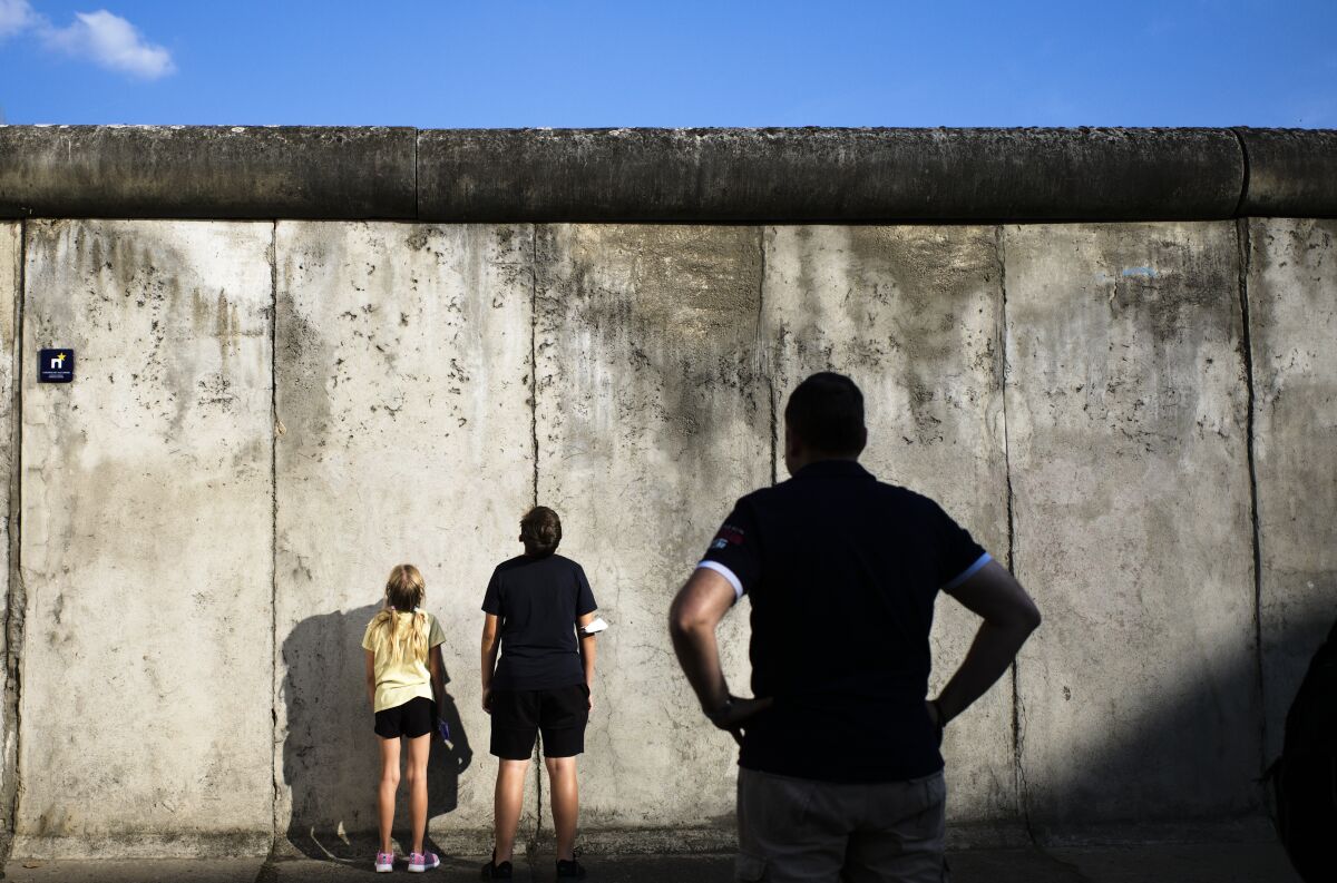 Visitors stand in front of remains of the Berlin Wall at the Wall memorial at Bernauer Strasse at the eve 60th anniversary of the construction of the Berlin Wall in Berlin, Germany, Thursday, Aug. 12, 2021. On Aug. 13, 1961 the East German government began constructing the Berlin Wall to split Berlin in an east and west part and marking a new step in the Could War between the western alliance and the communistic eastern block. (AP Photo/Markus Schreiber)