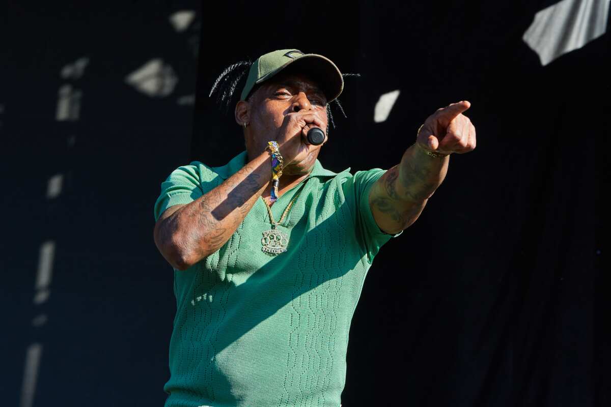 A man in a hat and green shirt sings into a microphone and points