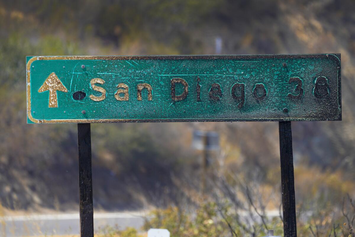 A road sign pointing toward San Diego is blackened by fire