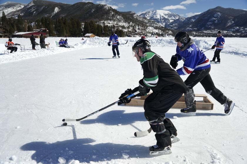 An athlete sweeps a puck behind a goal at a pond hockey tournament Saturday, Feb. 26, 2022, in Grand Lake, Colo. The event, which takes place on the state's largest natural lake, was held a month later than normal due to a delayed freeze following a trend of extremely hot summers and an uncharacteristically warm fall. (AP Photo/Brittany Peterson)