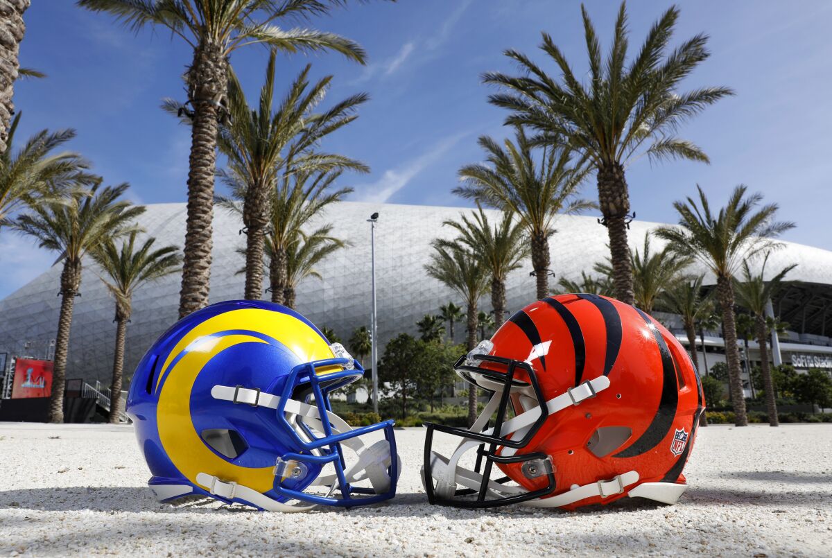 A Rams helmet and a Bengals helmet are pictured on the ground with palm trees in the background.