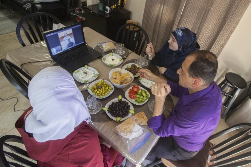 EL CAJON, CA - JANUARY 21: Eating a family meal, (from left) Huda Alsidnawi, Merfat Salas (mother), Khaled Alsidnawi (father), talk with Sami Labbad (on screen, above), Ahmad Alsidnawi (on screen, below) at their home on Thursday, Jan. 21, 2021 in El Cajon, CA. Ahmad and Sami are stuck outside the US. (Eduardo Contreras / The San Diego Union-Tribune)