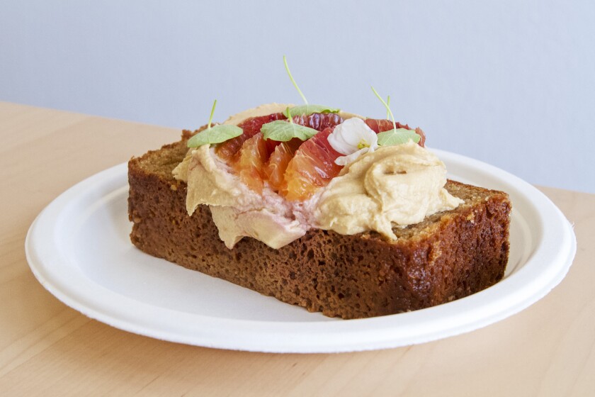 Una foto della torta da tè di Kala condita con glassa di formaggio cremoso, fette di arancia rossa e foglie di nasturzio.