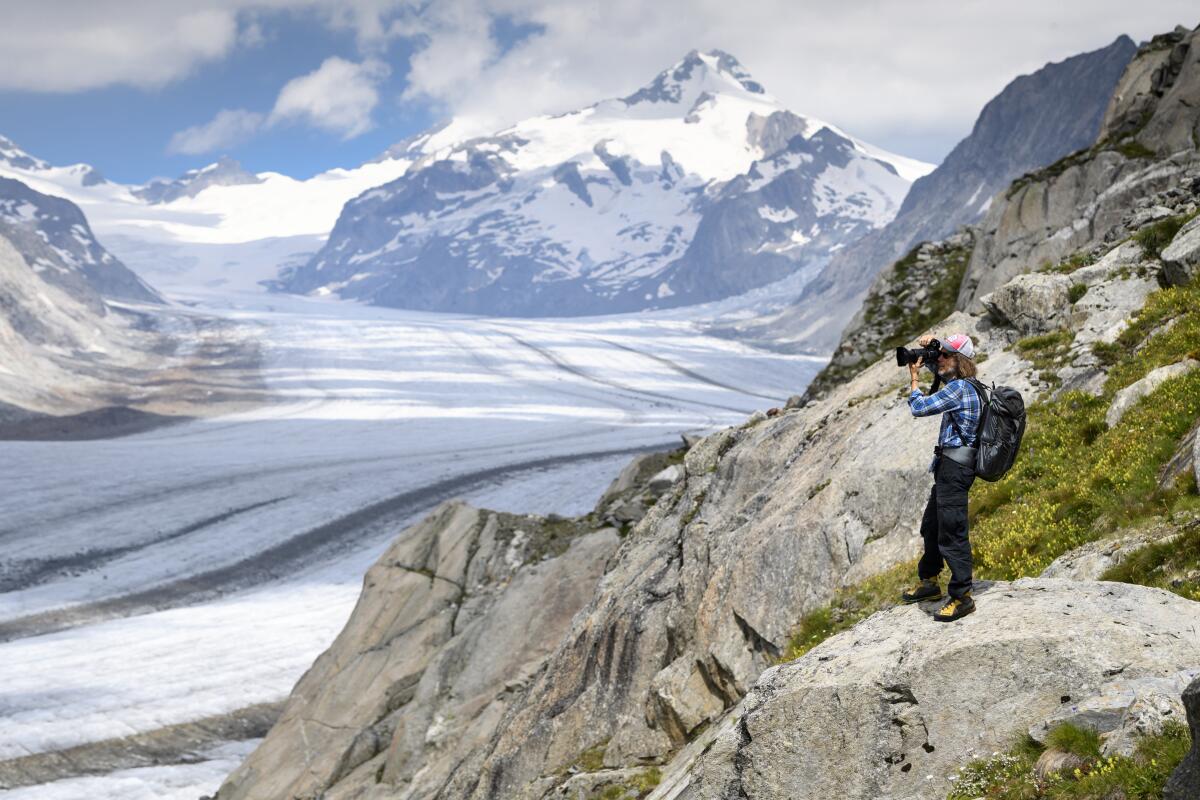 A person wearing a backpack photographs the Swiss Aletsch Glacier, the longest glacier in Europe.
