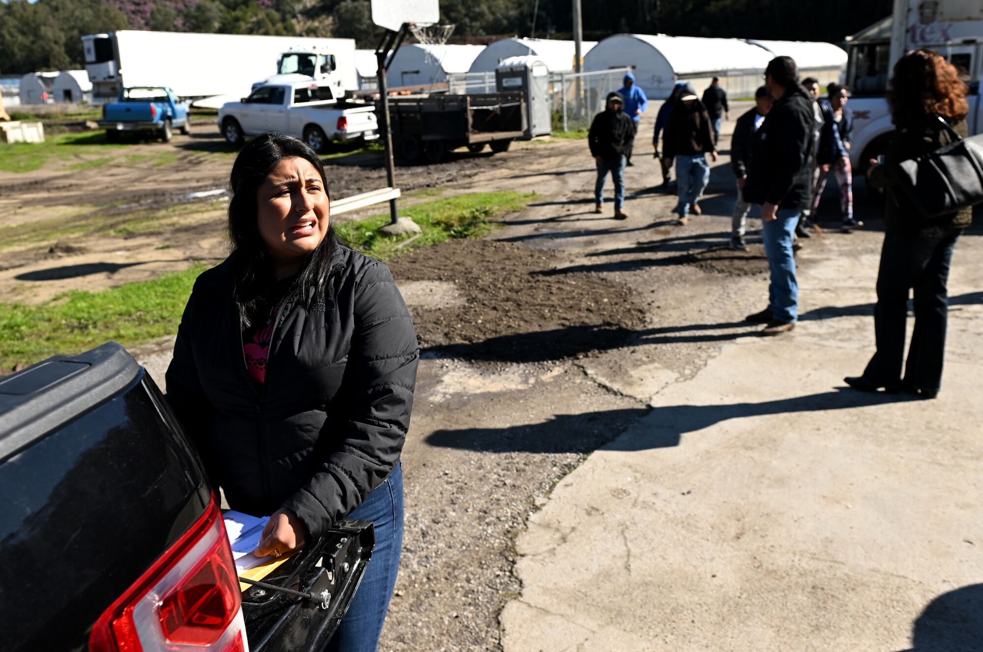 A woman stands at the open tailgate of a pickup as workers wait.