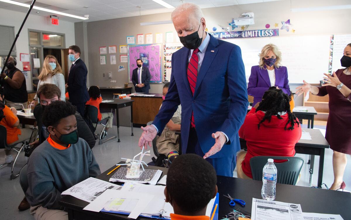 President Biden stands next to students working at a desk in a classroom