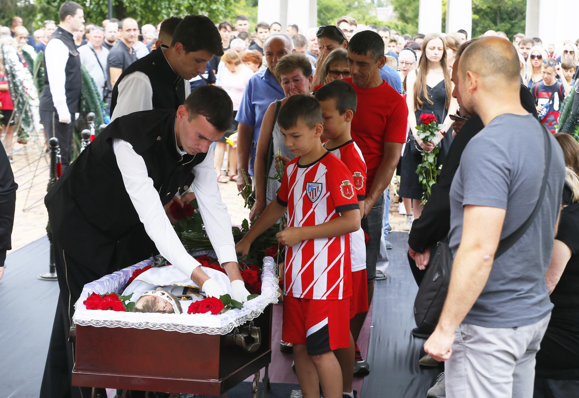 Friends, some wearing soccer jerseys, look at man in coffin.
