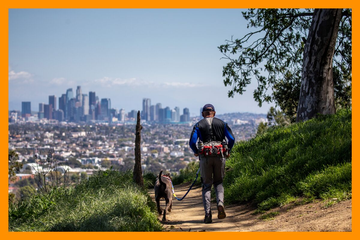 A man hikes with his dog on a trail in Kenneth Hahn State Recreation Area