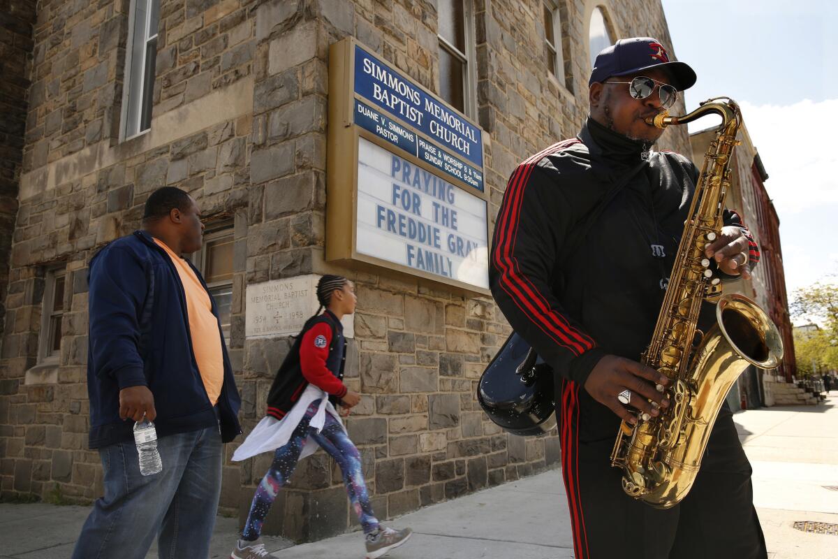 Prestis Vinson plays the saxophone in front of Simmons Memorial Baptist Church in Baltimore, where a sign shows support for Freddie Gray's family.