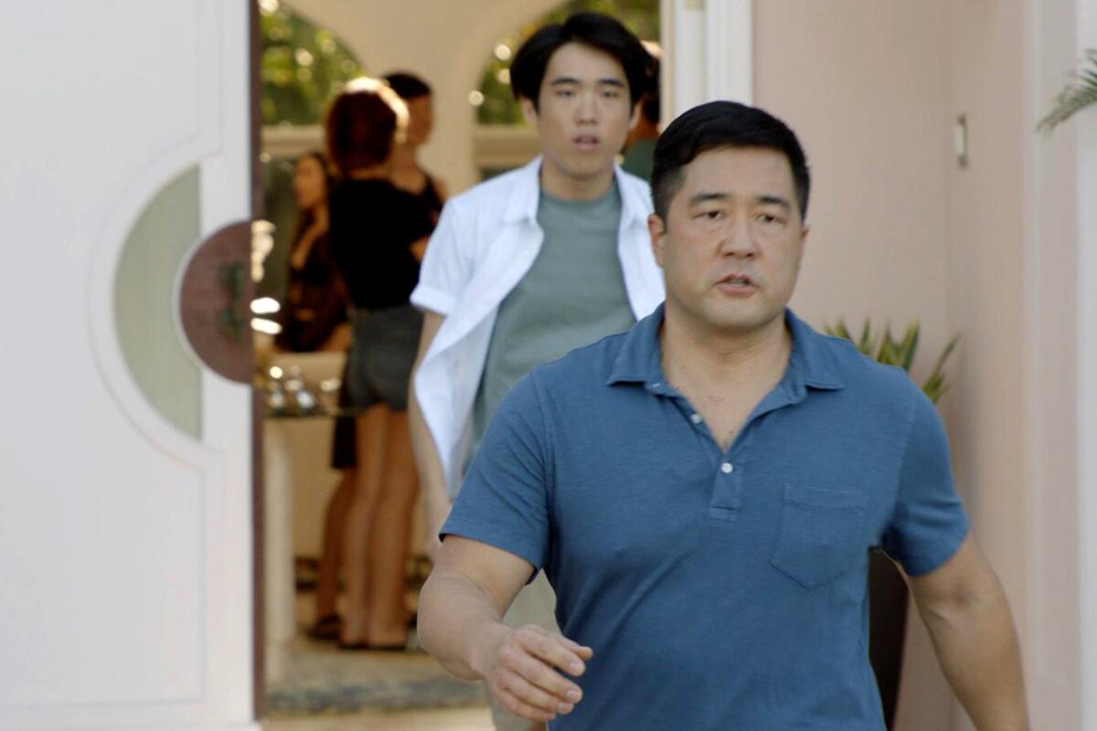 Two men walk out of a house in a scene from a TV show.