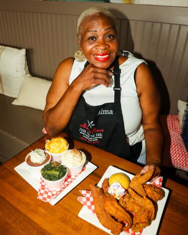 Alma’s Place Owner Alma Pleasant sits at a table with four side dishes and a platter of fried catfish and chicken