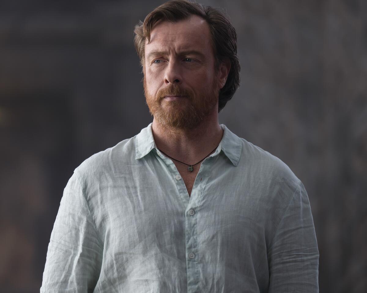 A man with red hair and a beard in a light blue shirt.