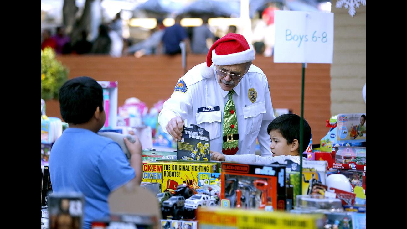 L.A. County Sheriff civilian volunteer Gary Jaegers helps six-year old Marco Gomez of Eagle Rock pick out a toy at the annual Crescenta Valley Sheriff's Station toy and food giveaway at Crescenta Valley Park in La Crescenta on Saturday, Dec. 16 2017.