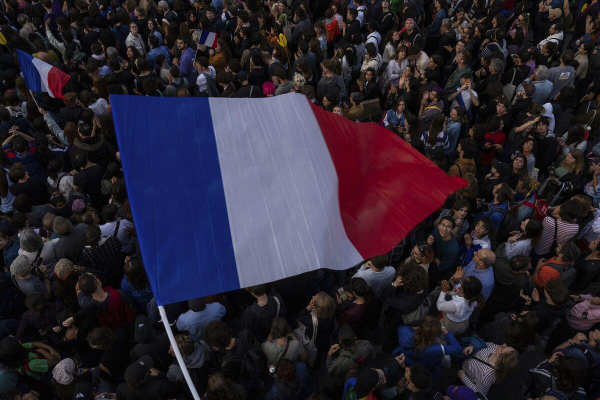 A large French flag waving above a crowd of people