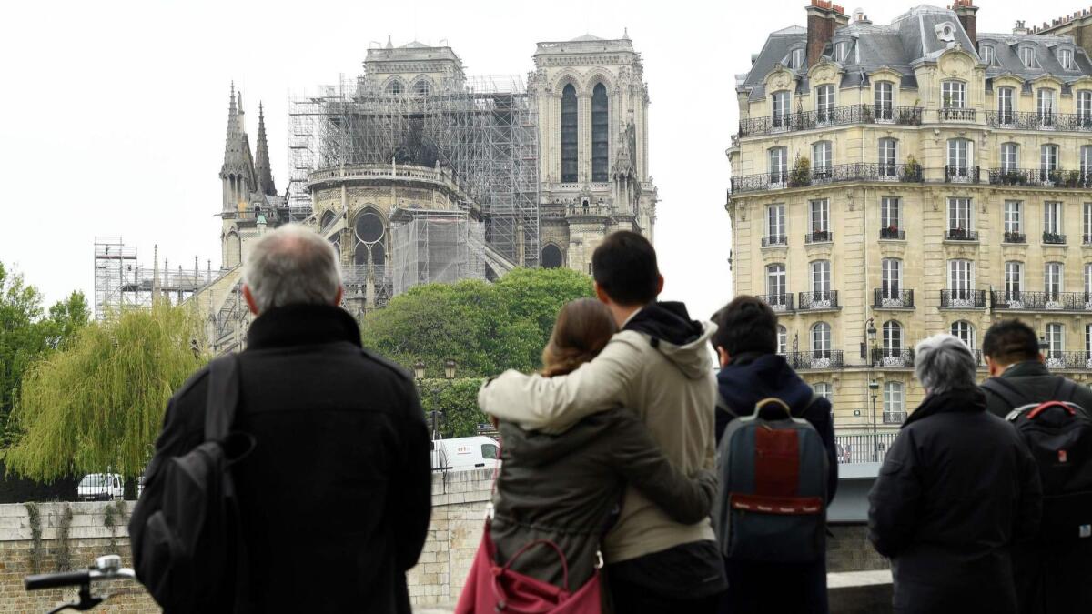 People hug while looking at Notre Dame on Tuesday in the aftermath of a fire that devastated the cathedral.