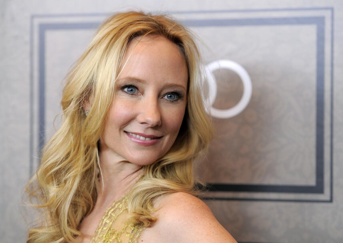 A woman with blond, curly hair smiles while looking over her shoulder.