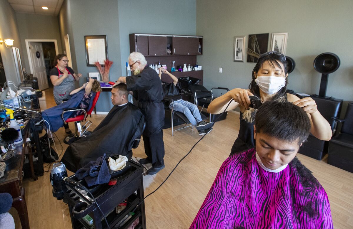 At the Hair Event in Fullerton, Kristy Rana, far left, threads Maureen Harry's eyebrows, salon owner Zaharia Bala cuts Ahmad Bitar's hair, center, and Kylee Liu cuts Anthony Arevalo's hair on Tuesday.