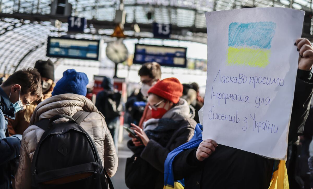 A woman holding a sign waits with a crowd for Ukrainians  arriving at the main train station in Berlin.