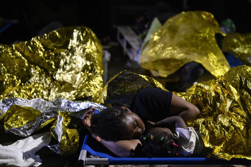 A woman and a child sleep outside the Lampedusa's migrant reception center, Sicily, early Thursday Sept. 14, 2023. The reception center in Italy's southernmost island of Lampedusa remained critical Thursday as it coped with transferring to the mainland thousands of migrants who arrived on small, unseaworthy boats in a 24-hour span this week. (AP Photo/Valeria Ferraro)