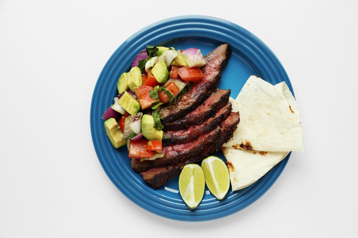 Sliced grilled steak, guacamole salad, lime slices and tortillas on a blue plate