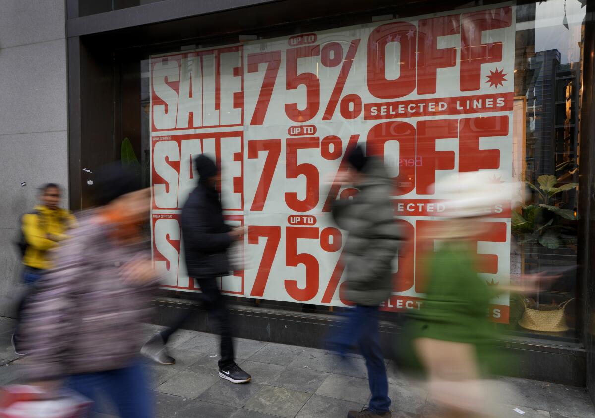 Shoppers pass a window displaying a sale sign