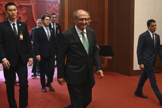 A man in dark suit and green tie walks in front of other men, in dark suits and ties