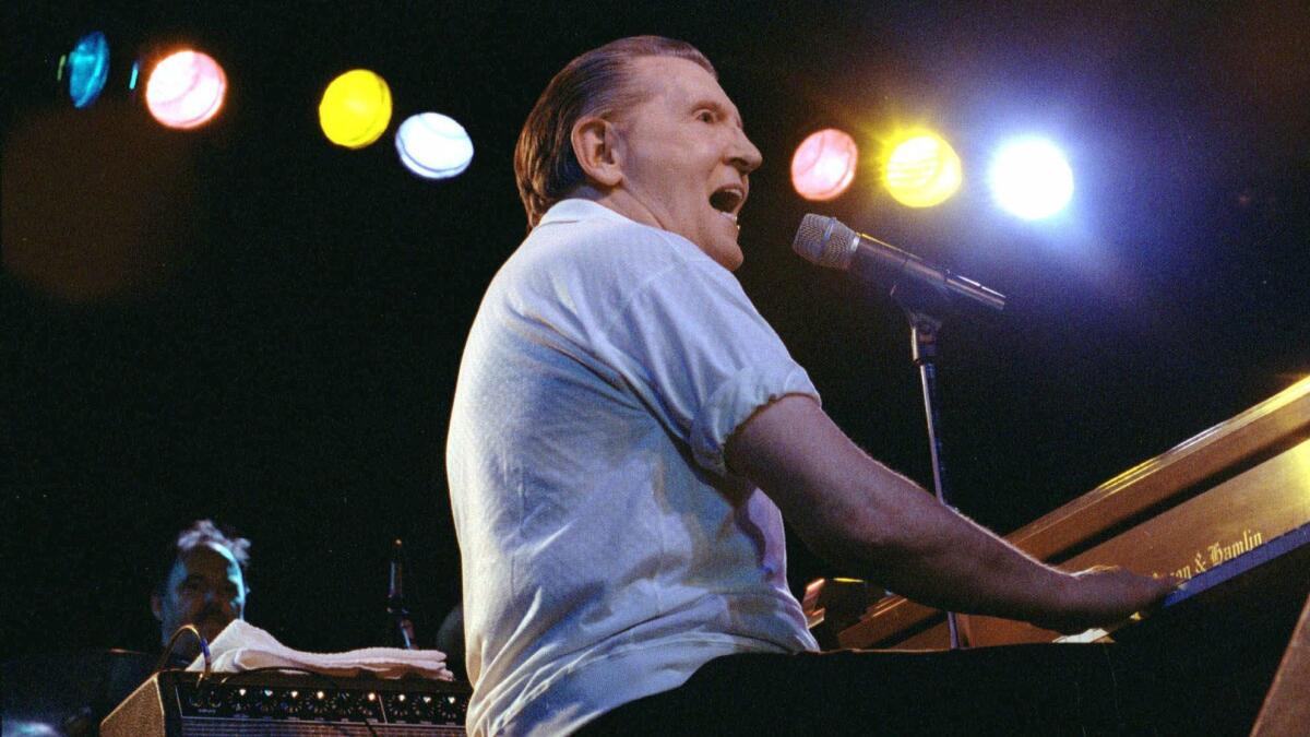 Jerry Lee Lewis, seated at the piano before a microphone, performs. 