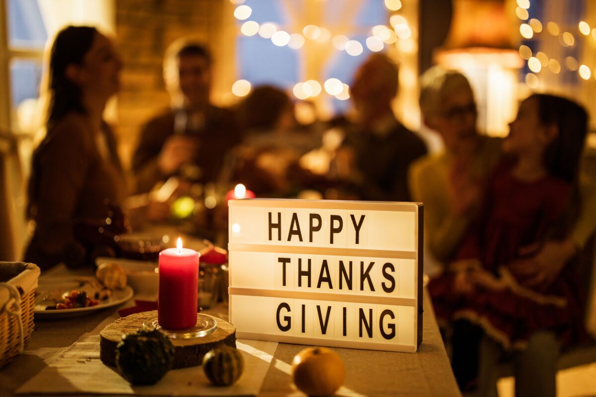 A sign with 'Happy Thanksgiving' on dining table with people in the background.