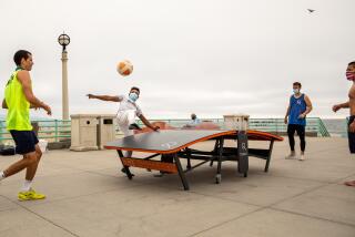 MANHATTAN BEACH, CA - AUGUST 24: Antonio Medina, center in gray, prepares to set up his teammate Andres Berriel, left, during a game of Teqball, against Brett Lorenzini, blue tank and Ryo Mizushima, right, on the Manhattan Beach, CA Pier, Monday, Aug. 24, 2020. The naturally socially-distant game, Teqball is played on a curved table, in single or doubles format, combining the sports of soccer and table tennis, where no hands or arms can be used. Berriel and Lorenzini are members of the L.A. Teqers teqball team, who, along with other team members, travel around the L.A. area setting up the table as ambassadors of the sport that is played internationally. (Jay L. Clendenin / Los Angeles Times)