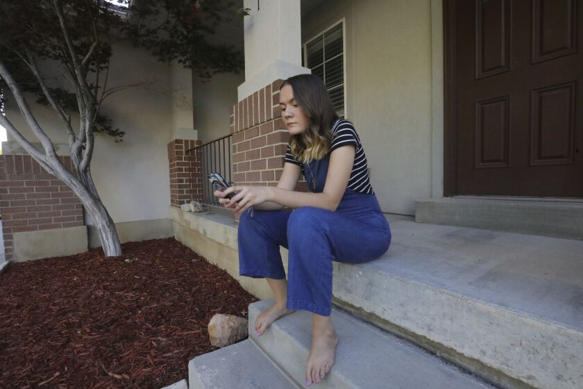In this Monday, July 22, 2019, photo, Rachel Whalen looks at her phone at her home in Draper, Utah. Whalen remembers feeling gutted in high school when a former friend would mock her online postings, threaten to unfollow or unfriend her on social media and post inside jokes about her to others online. The cyberbullying was so distressing that Whalen even contemplated suicide. There's a rise in cyberbullying nationwide, with three times as many girls reporting being harassed online or by text message than boys, according to the National Center for Education Statistics. (AP Photo/Rick Bowmer)
