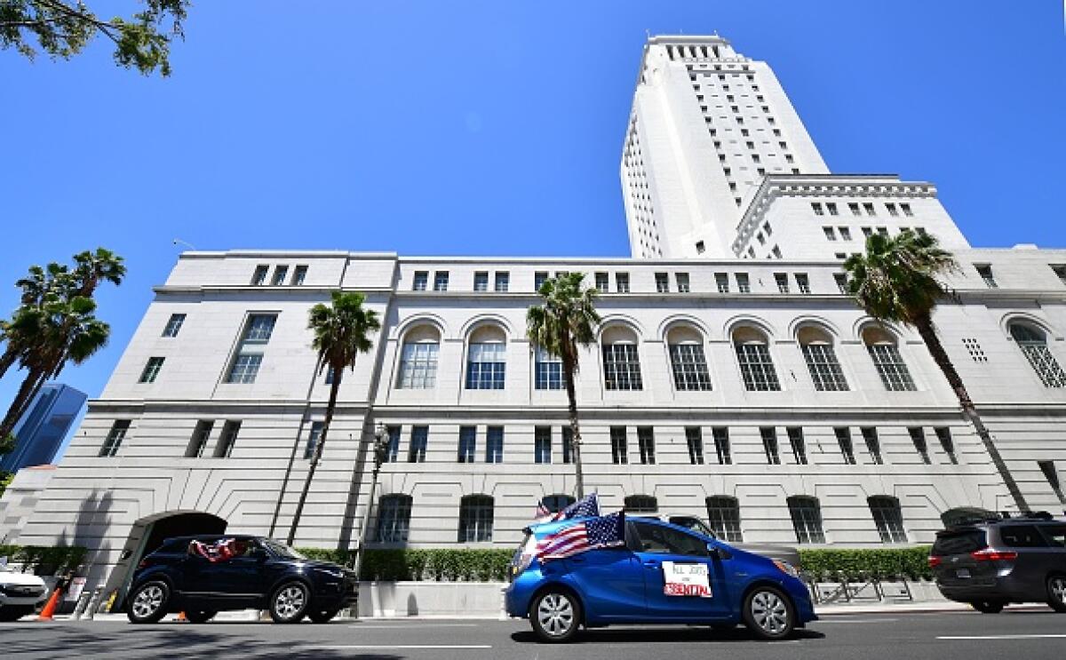 Cars drive past a white building with a tower and palm trees in front 