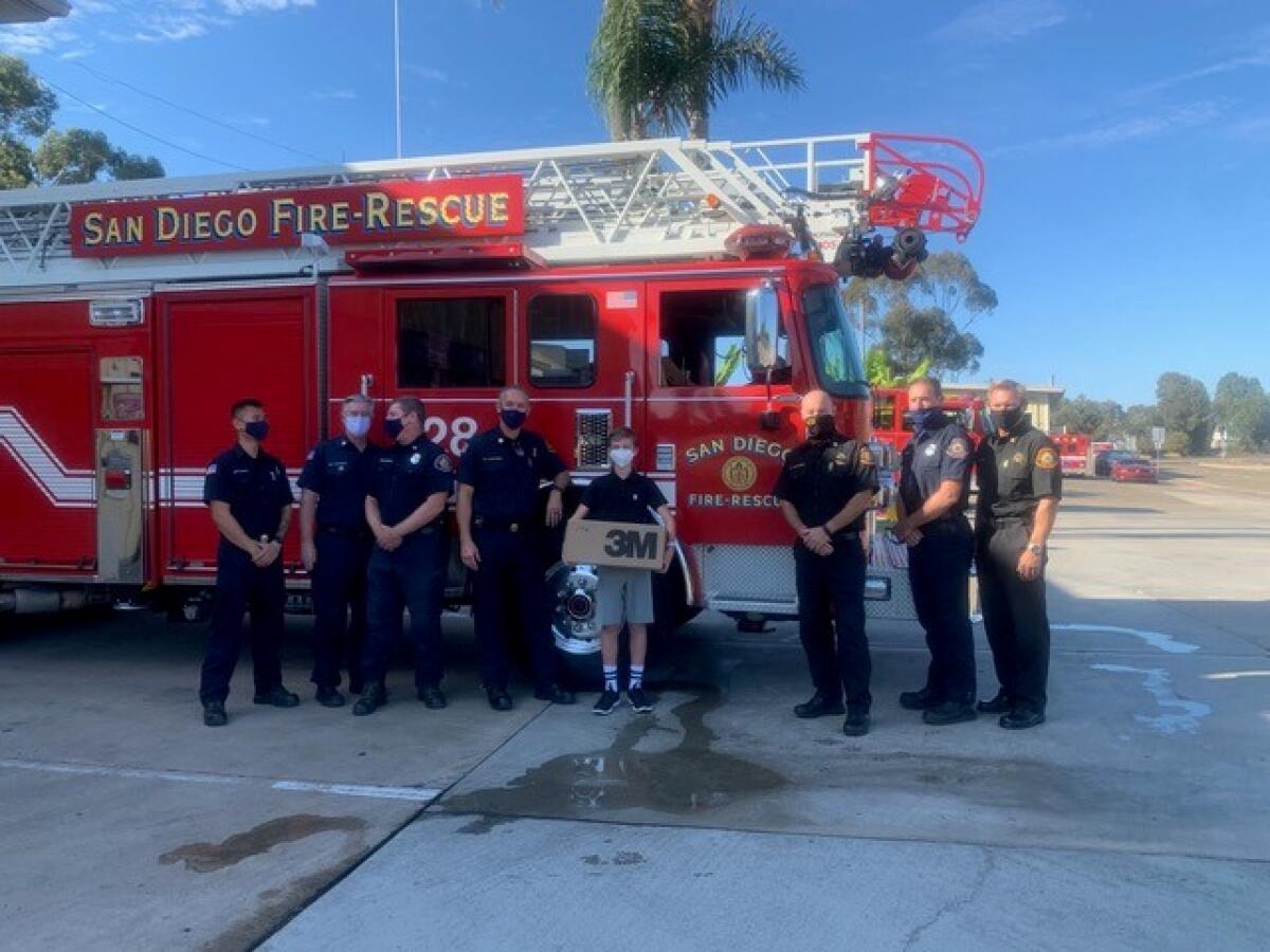 Bishop’s School eighth-grader Ezra Granet stands with firefighters after donating 10,000 masks to San Diego Fire-Rescue.